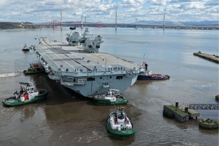 HMS Queen Elizabeth guided by tugs, having just emerged from the Rosyth yard’s basin, with the Forth Bridges in the background.